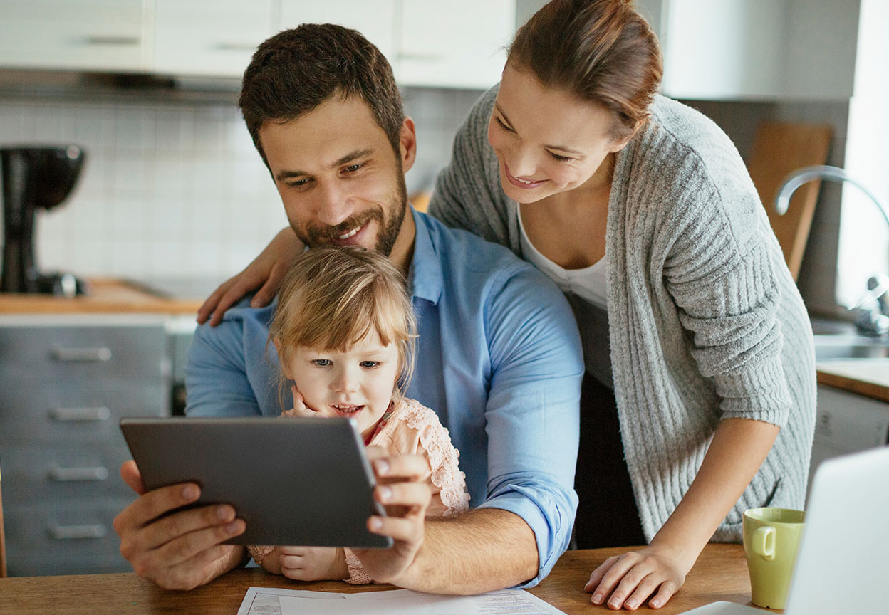 A family in the kitchen looks at a tablet together at the table