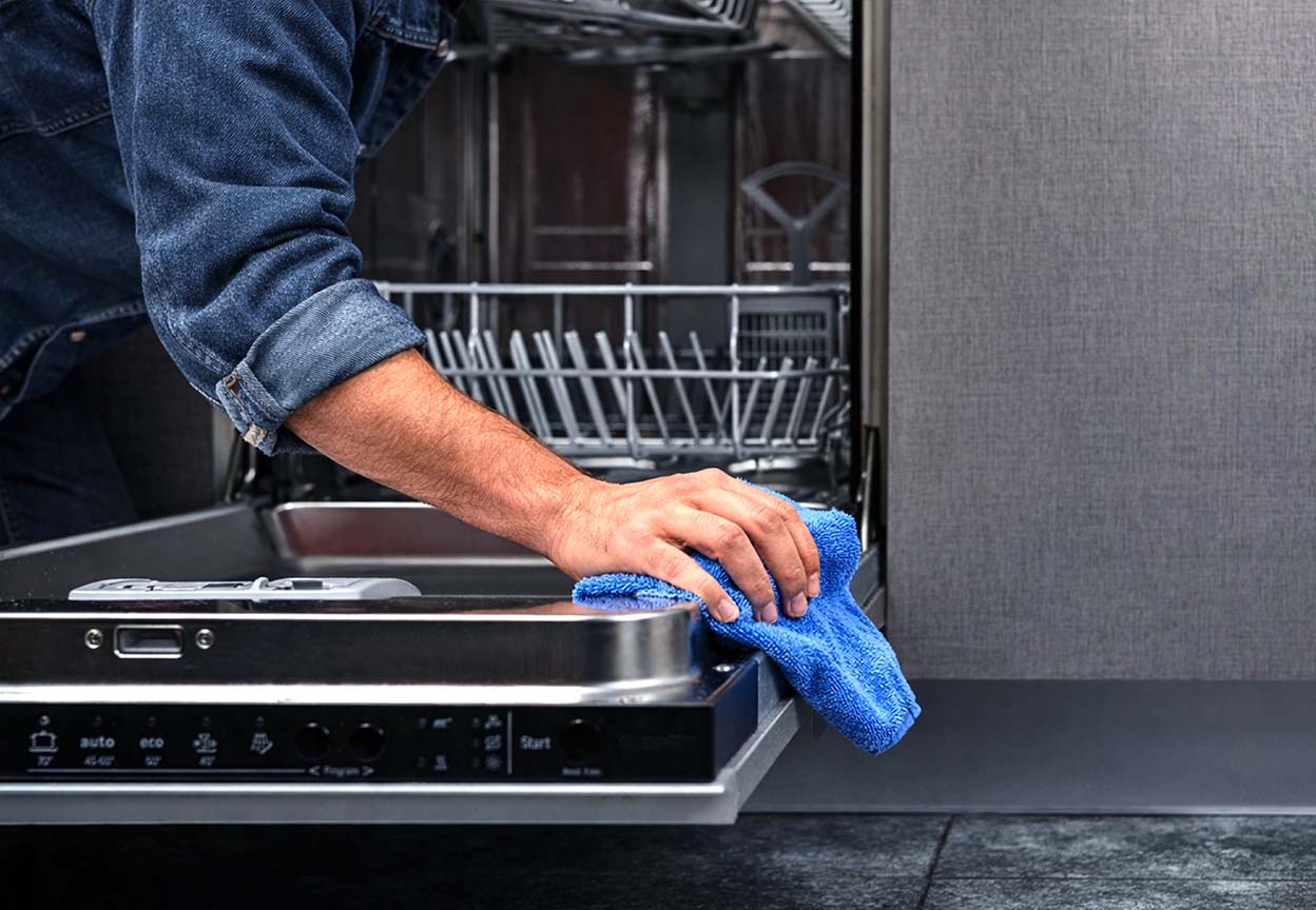 Person wipes the edge of an open dishwasher door with a blue microfiber cloth