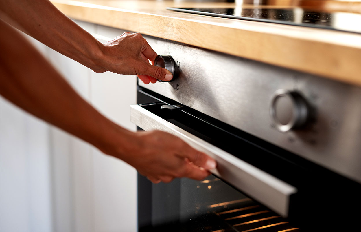 Close-up of someone turning the knob and opening a stainless steel oven door in a kitchen
