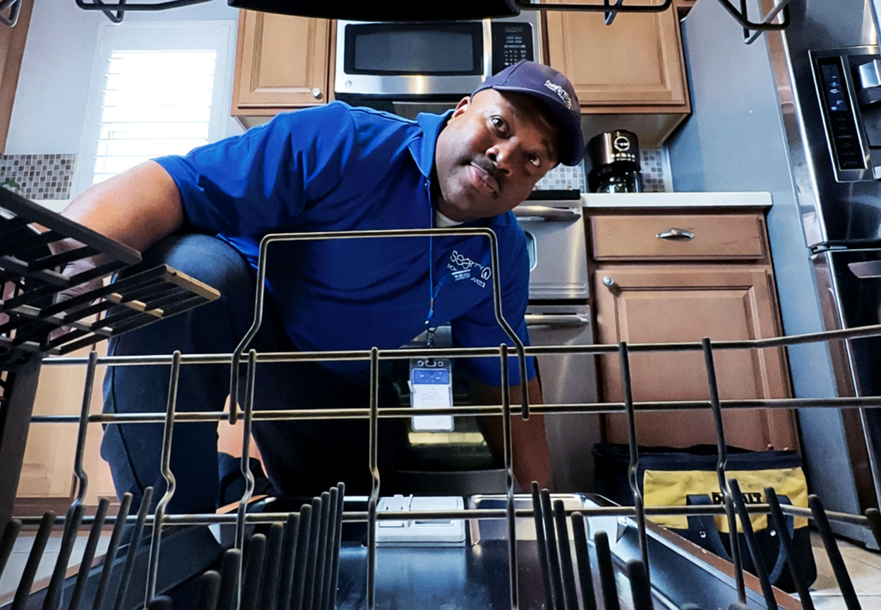 A Sears appliance technician leans into an open dishwasher to inspect the interior racks and components