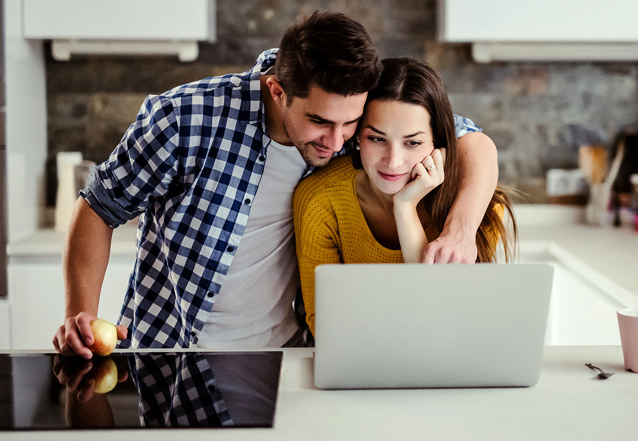 A couple reviews information on a laptop together at a kitchen counter