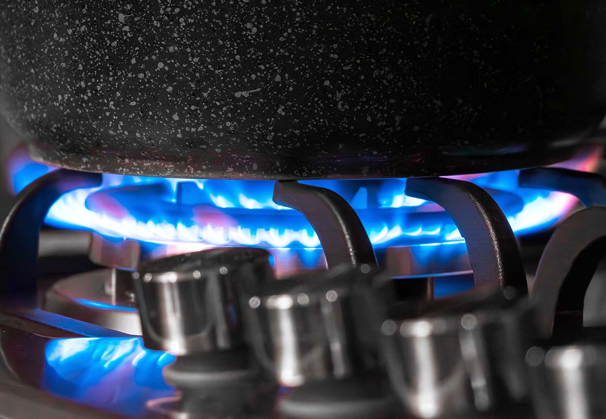 Close-up of a pot heating on a gas stove with bright blue flames visible beneath the burner grate