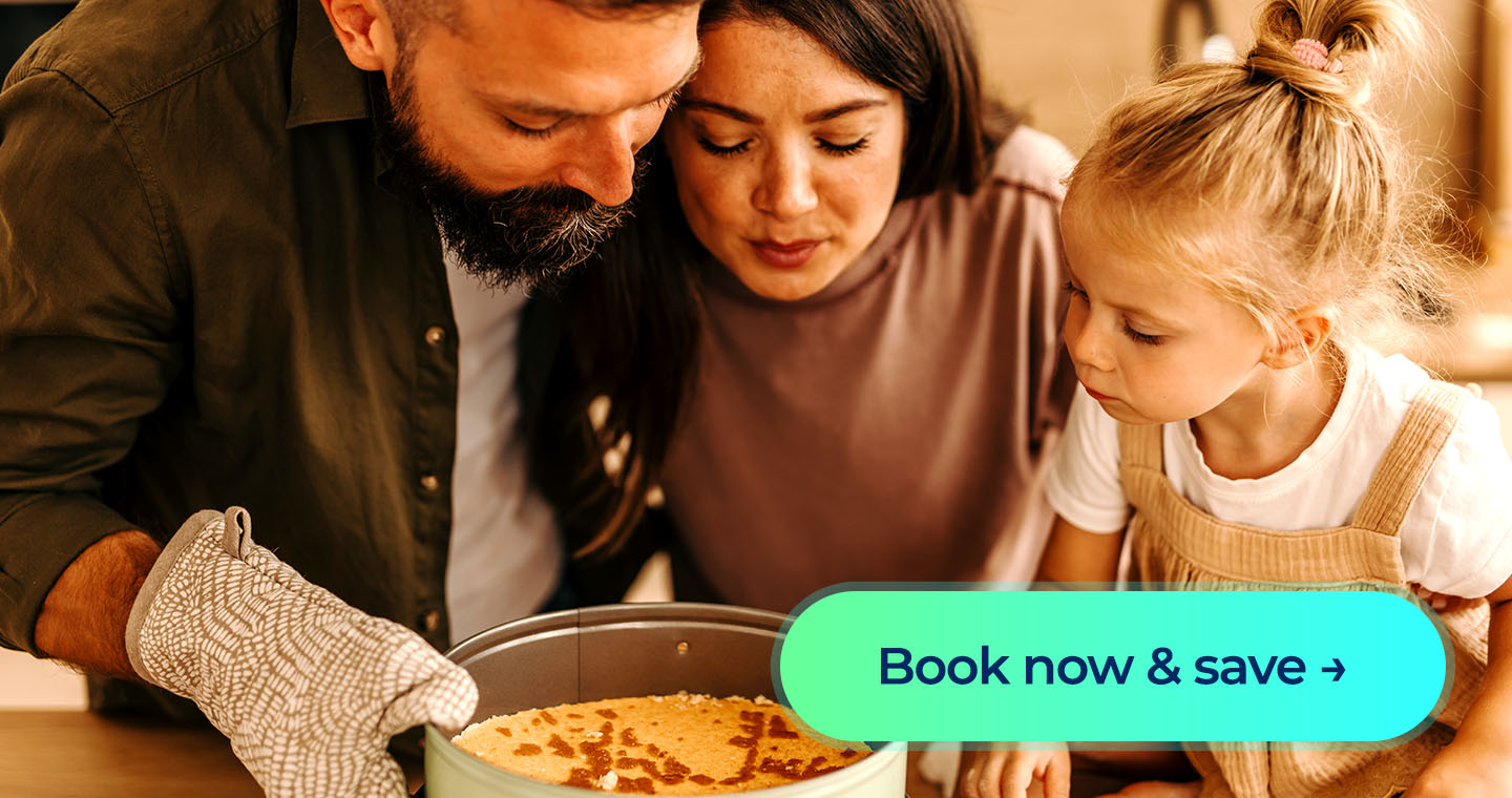 Family leaning over a kitchen counter as a parent carefully lifts a freshly baked cake from the oven while a young child watches closely