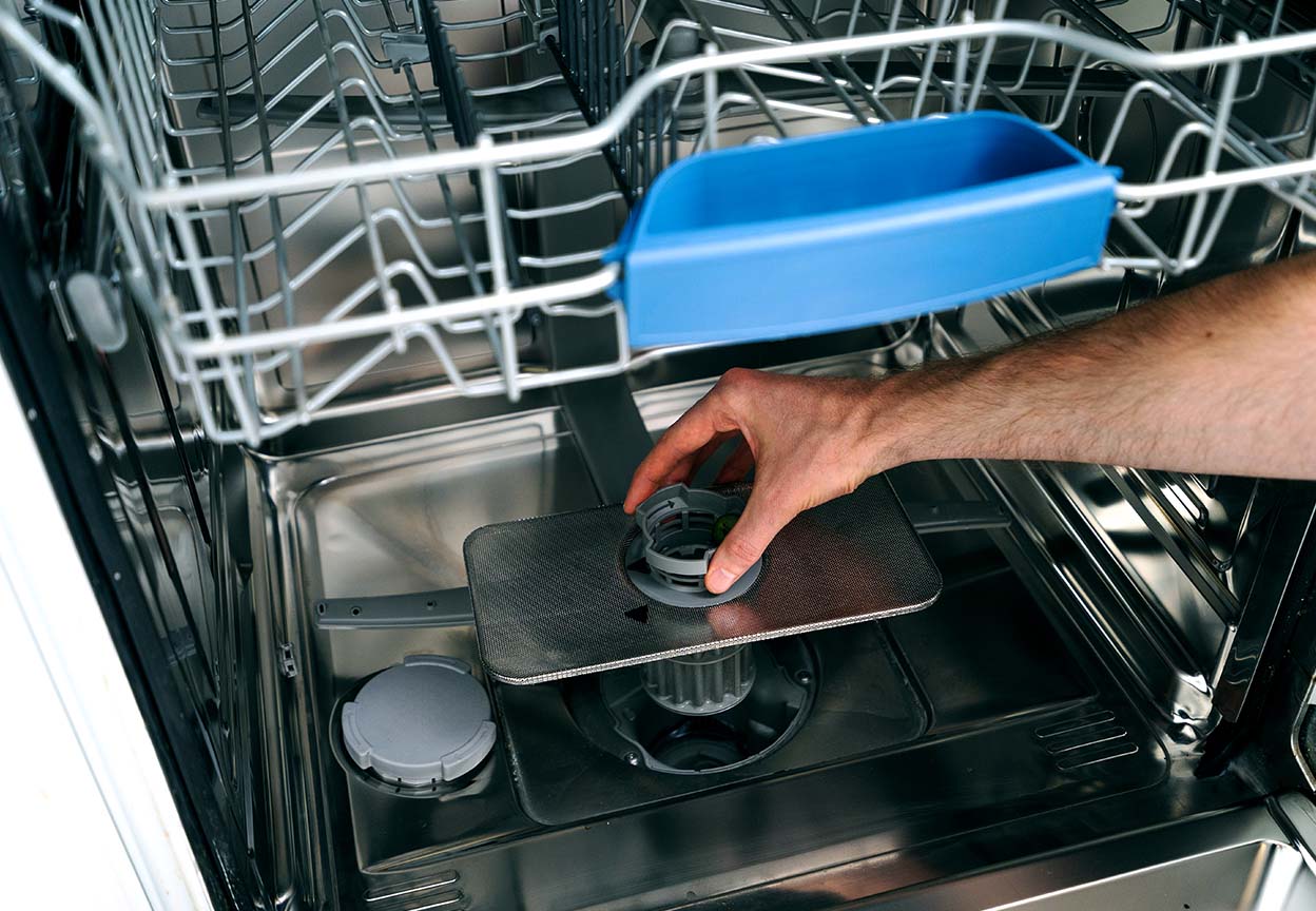 Dishwasher rack with person pulling out a filter showing how loading mistakes and clogged filters can lead to dishes coming out less clean
