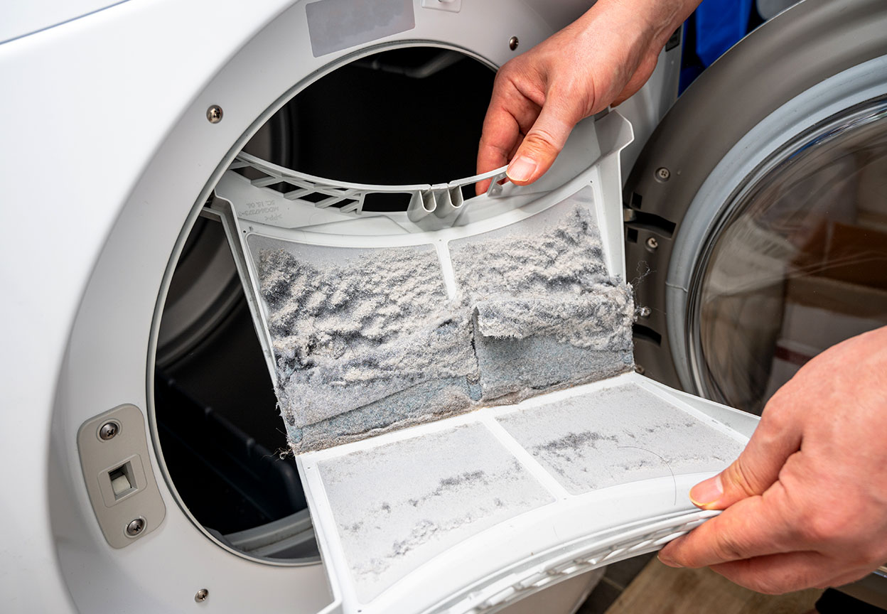 A person cleaning a lint trap within a dryer and while showing mounds of lint on top