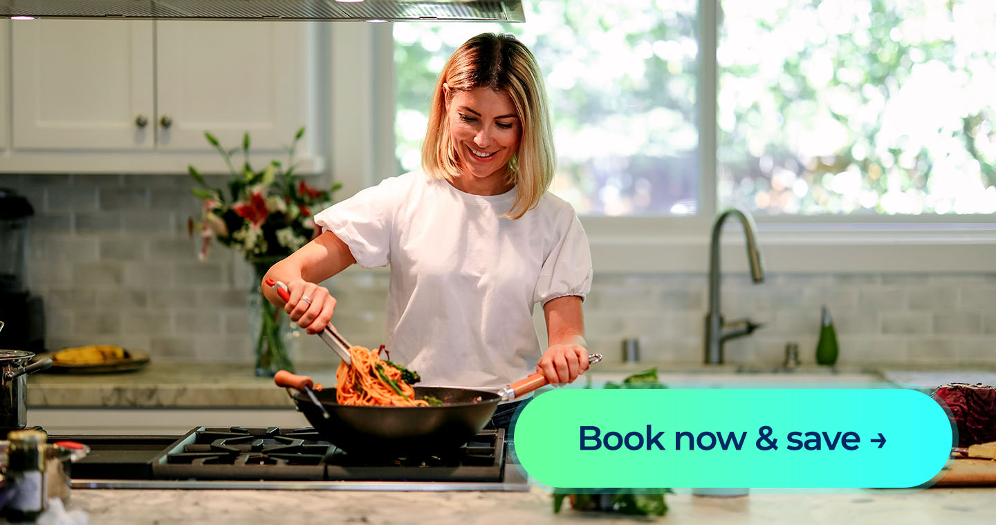 A woman cooks dinner over a large stovetop in a modern kitchen with white cabinets and light grey tiles