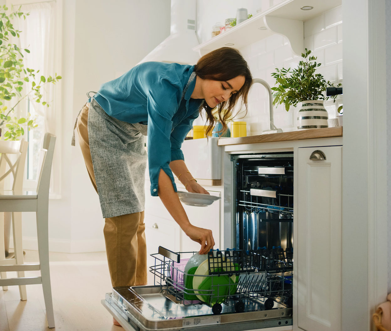Woman loading dishes into an open dishwasher in a bright kitchen