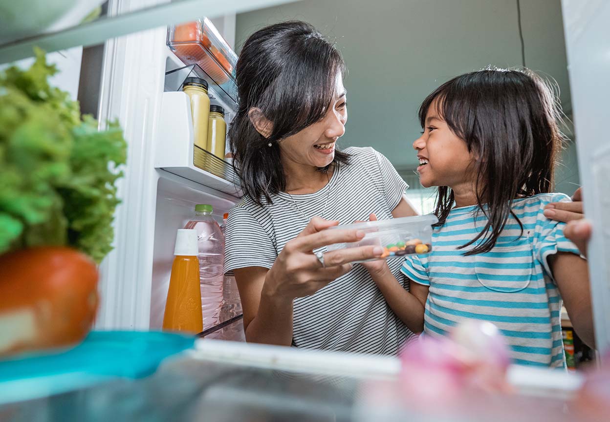 Adult and child smiling together while choosing food from an open refrigerator