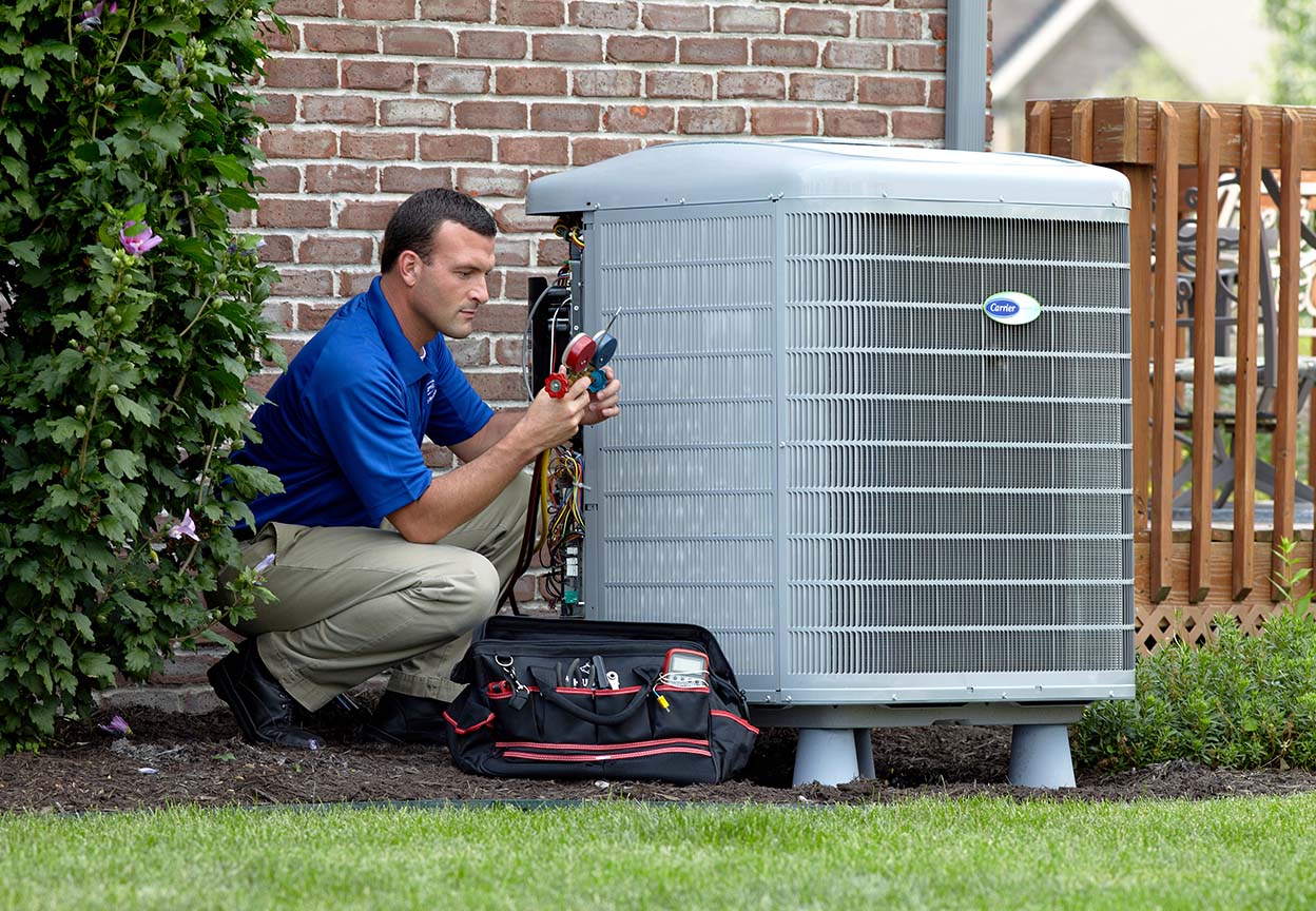 Technician servicing an outdoor air conditioning unit beside a brick home