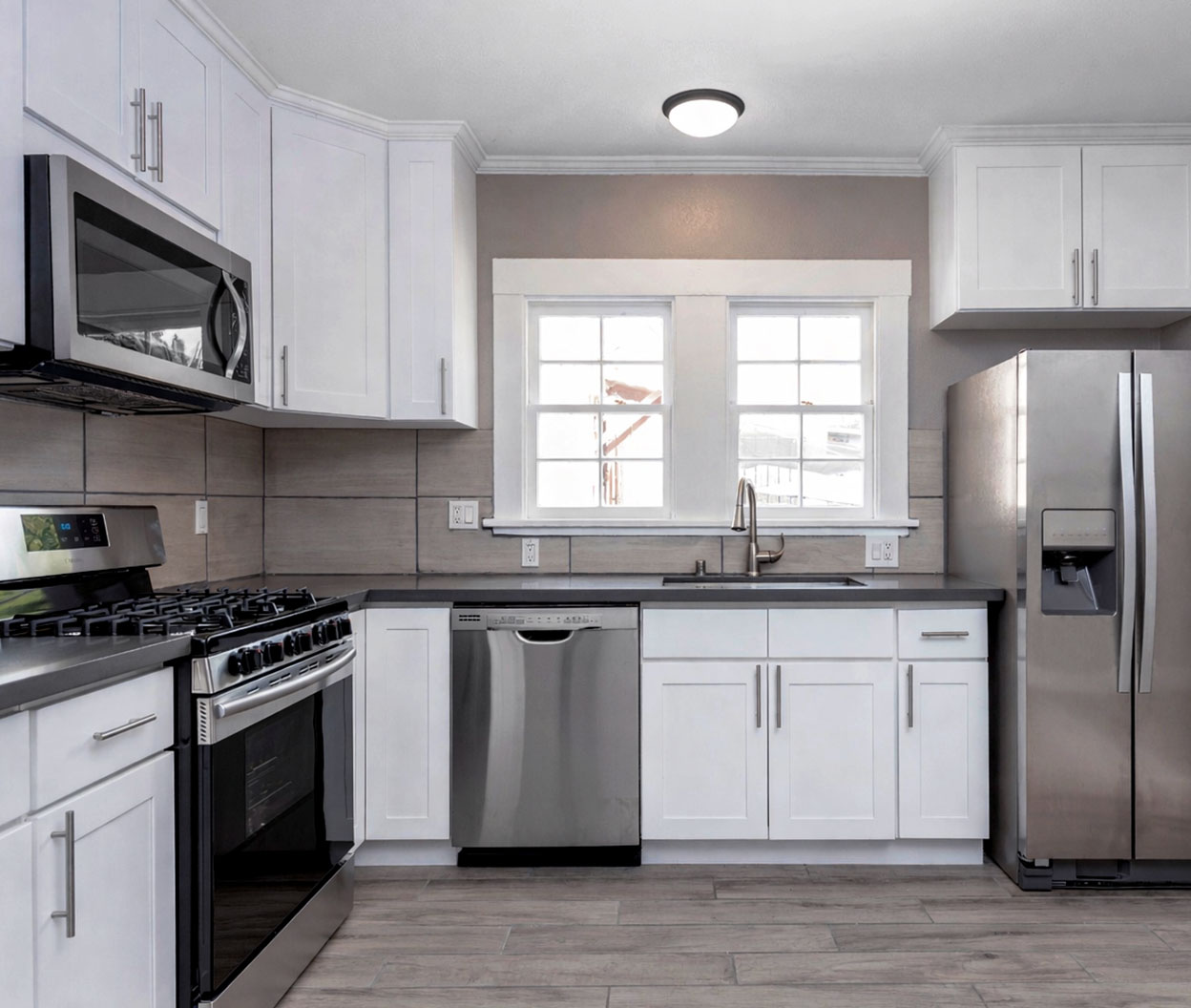 Bright modern kitchen with white cabinets and stainless steel appliances including a stove, microwave, dishwasher, and refrigerator