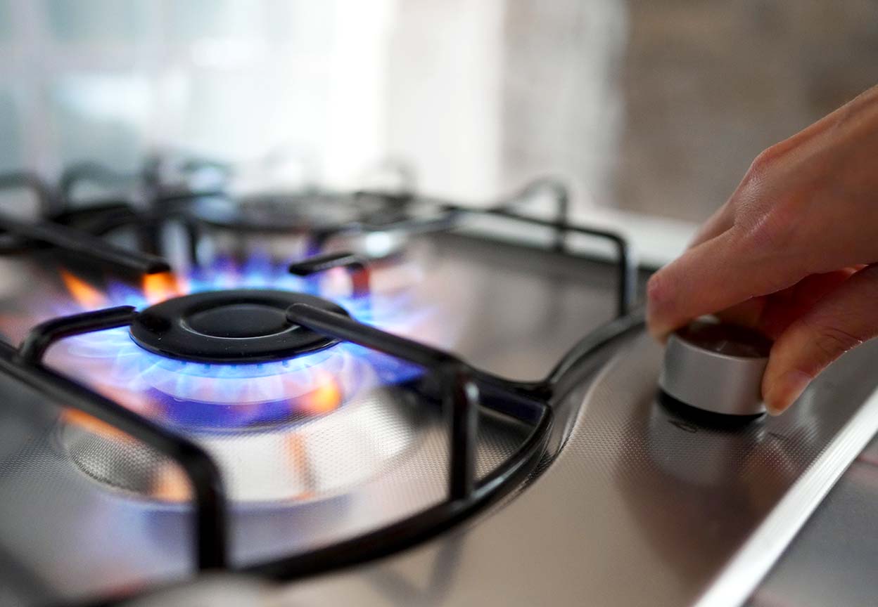 Close-up of a hand turning the knob on a lit gas stove burner