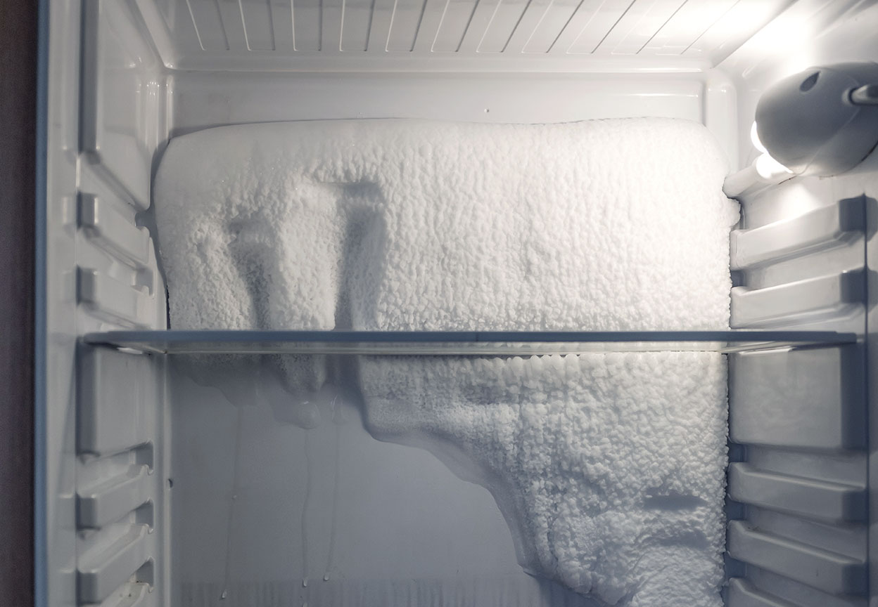 Heavy ice buildup blankets the back wall of a freezer compartment beneath a glass shelf