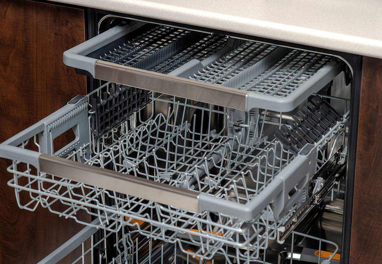 An open dishwasher shows its empty racks and utensil tray ready for loading