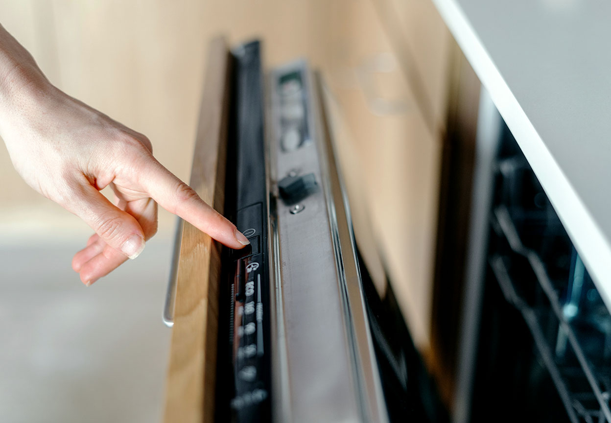 A person presses a setting on the control panel of a built-in dishwasher
