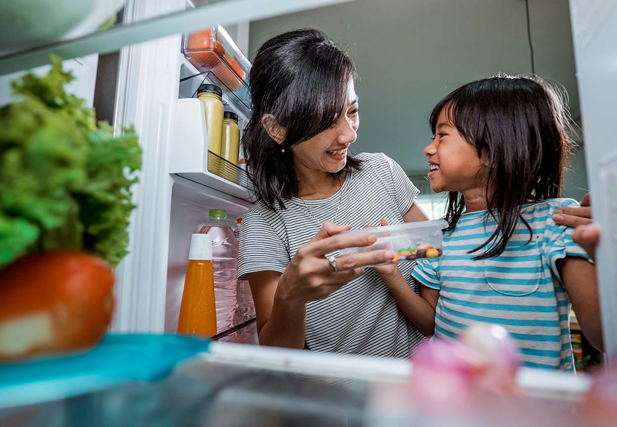 Parent and child smiling while choosing food from the refrigerator