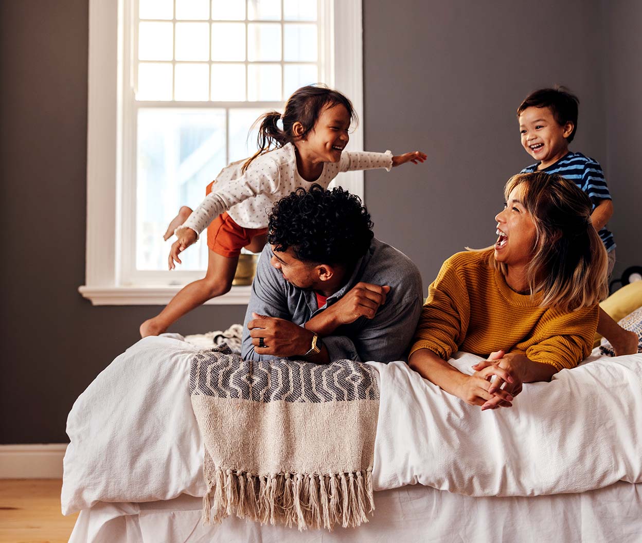 A family laughs and plays together on a bed in a bright bedroom