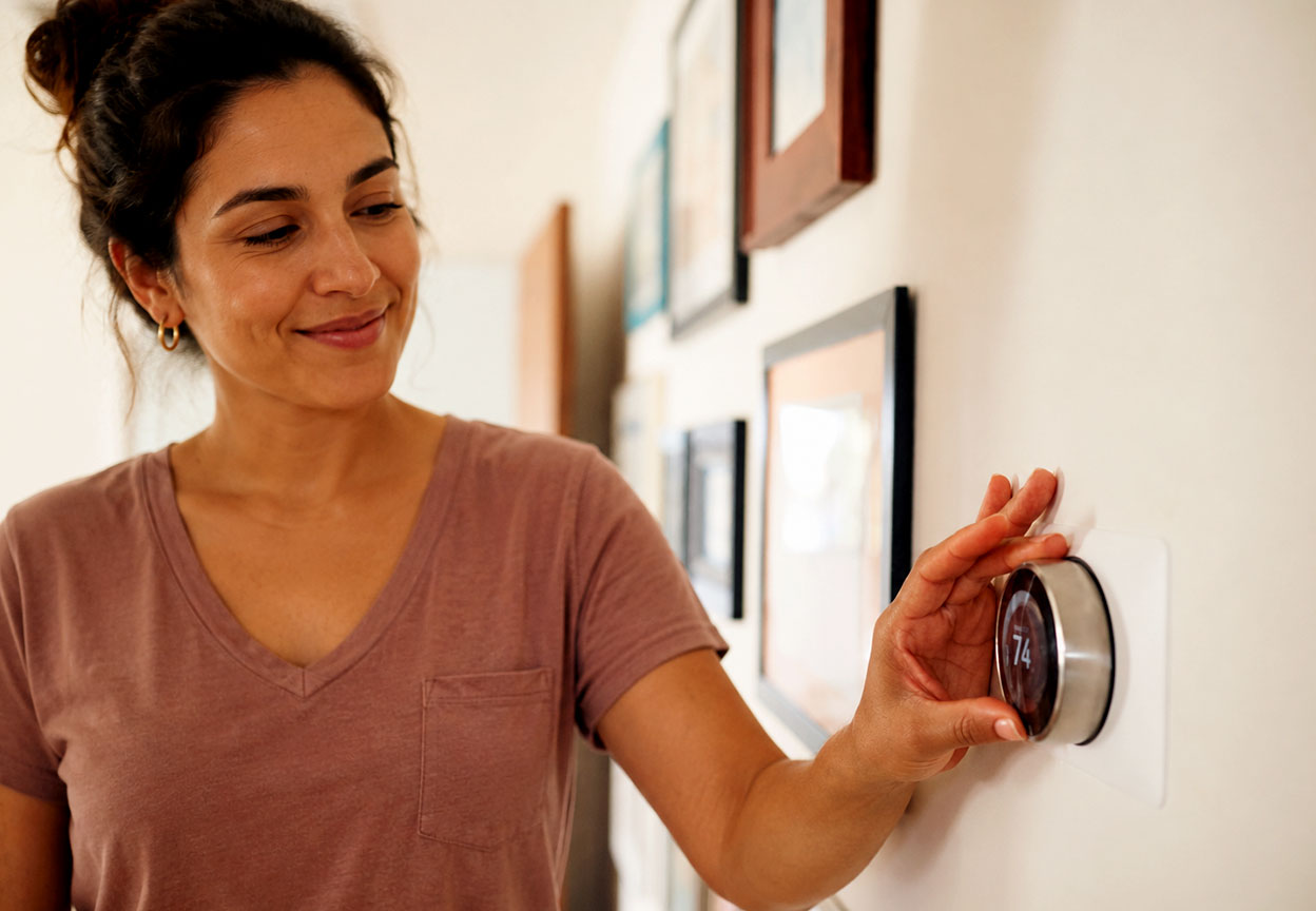 A woman adjusts a thermostat to help keep her home comfortable