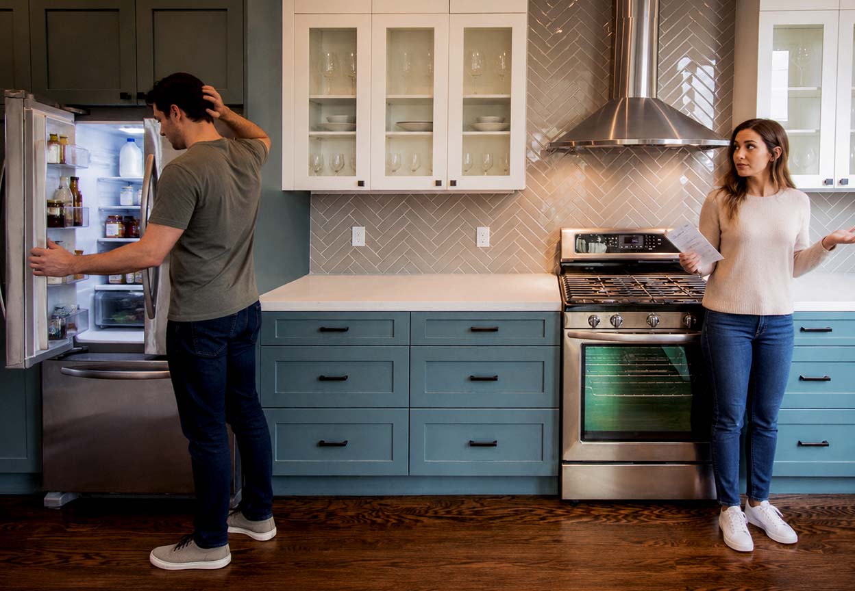 Homeowners look over paperwork while checking a refrigerator in a kitchen
