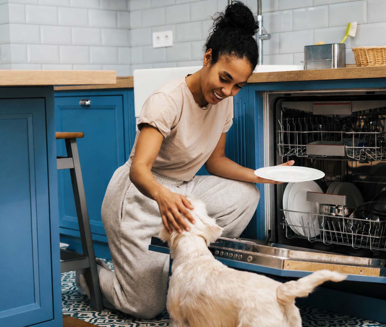 Woman petting her dog while removing dishes from an open dishwasher