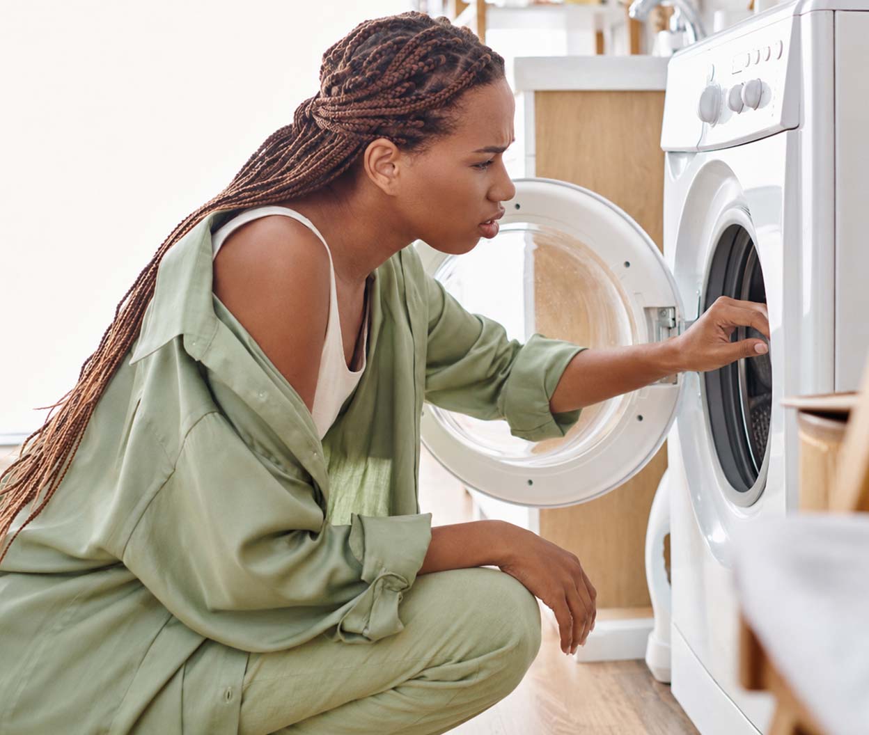 Woman crouches beside an open washer while checking the inside of the machine