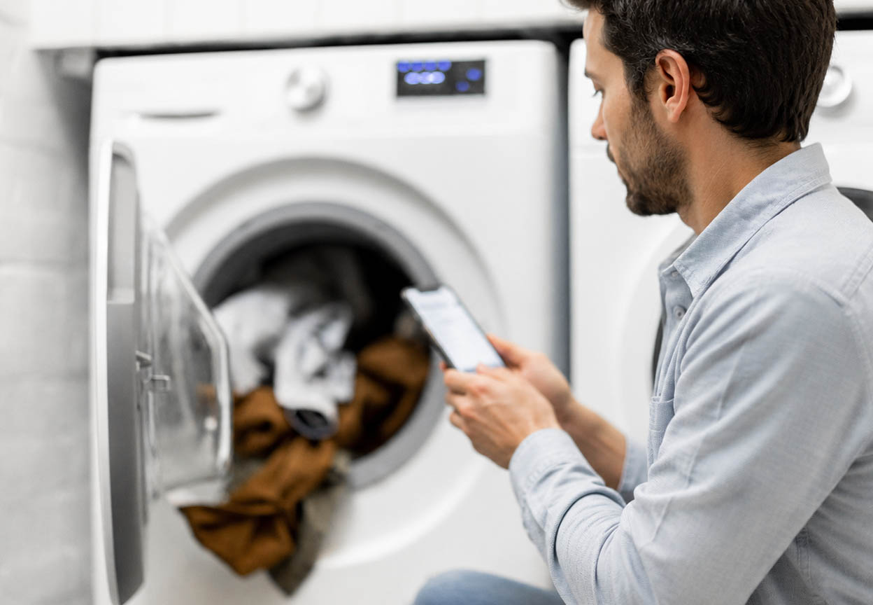 Man checks his phone beside an open dryer containing a load of laundry