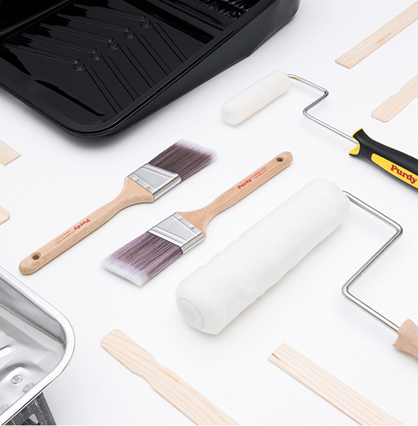 Purdy paint brushes & rollers, stir sticks and painting trays arranged on a white surface.