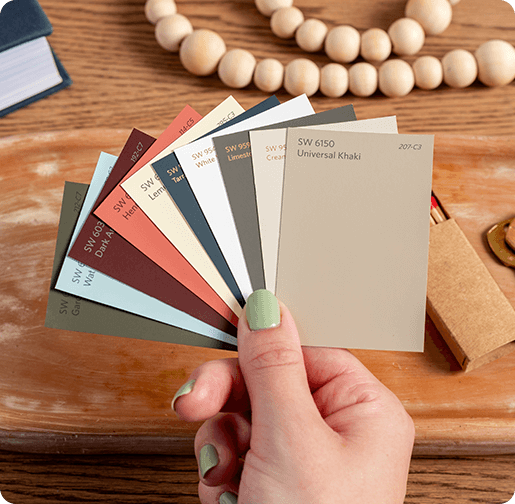 Hand holding color chips, including Universal Khaki, over wood table with other materials.