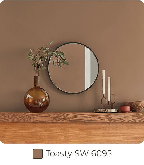 Home decor and mirror on medium wood ledge in front of wall painted in Toasty SW6095.