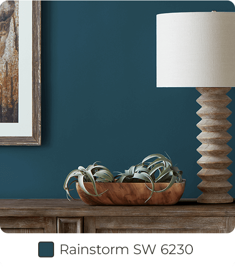 Plants in breadbowl, with lamp and hanging frame, on dark wood furniture in front of wall painted in Rainstorm SW6230.