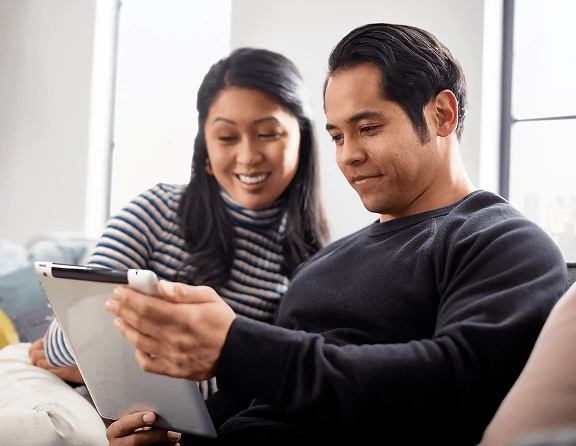 Couple sitting together on sofa while looking at a tablet.