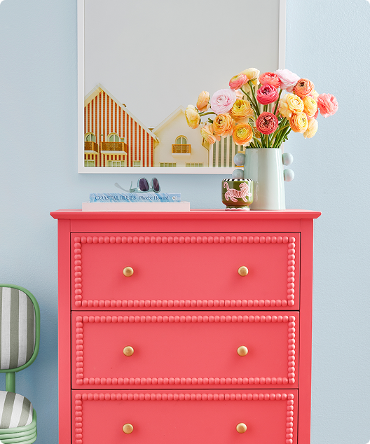 Salmon colored dresser with white planter and objects in front of blue wall.