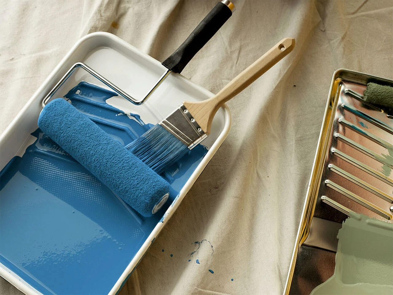 A paint brush and roller on a painting tray with blue paint.