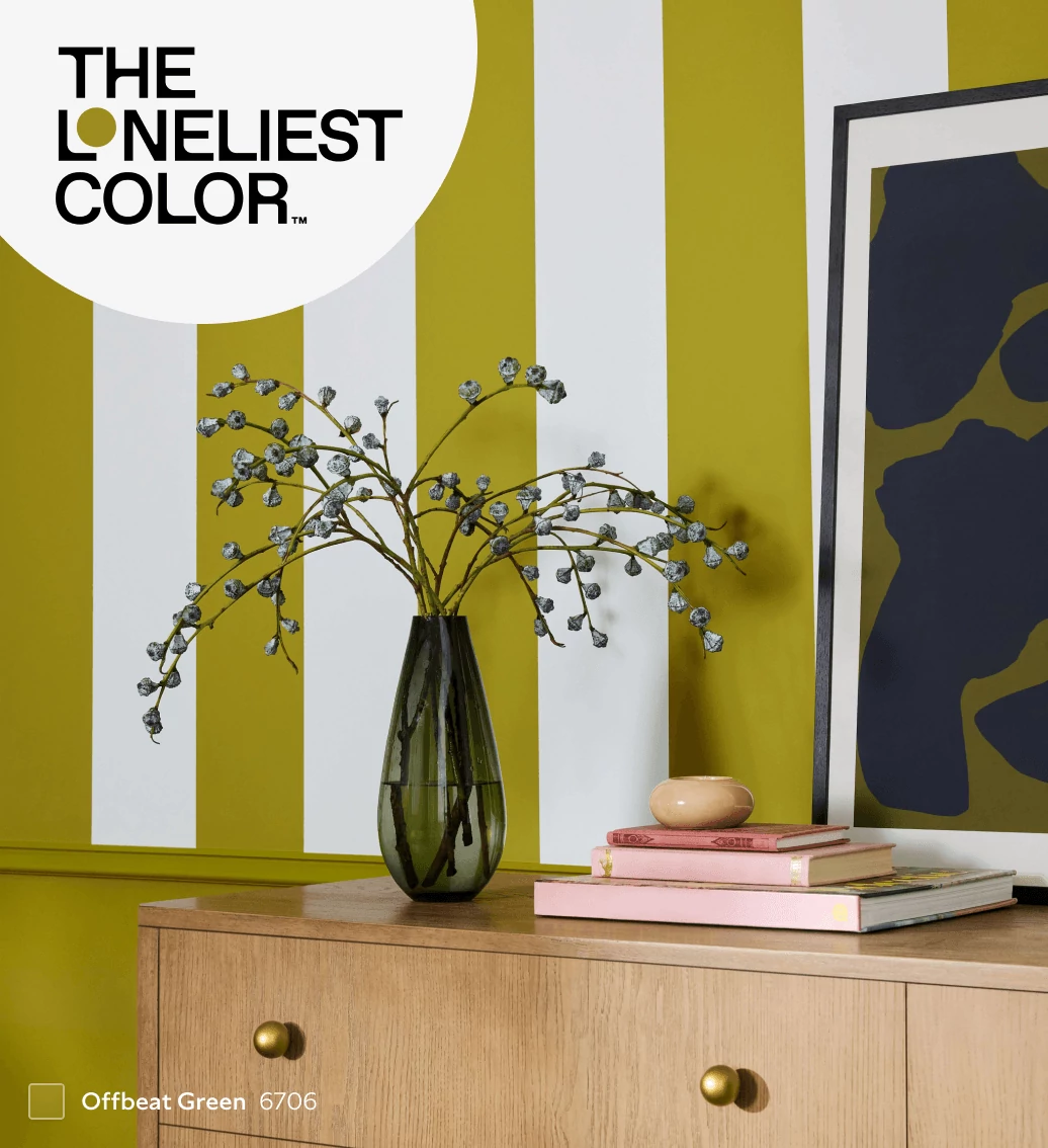 The Loneliest Color™. Offbeat Green painted striped wall behind blond wood console table with home decor on top.