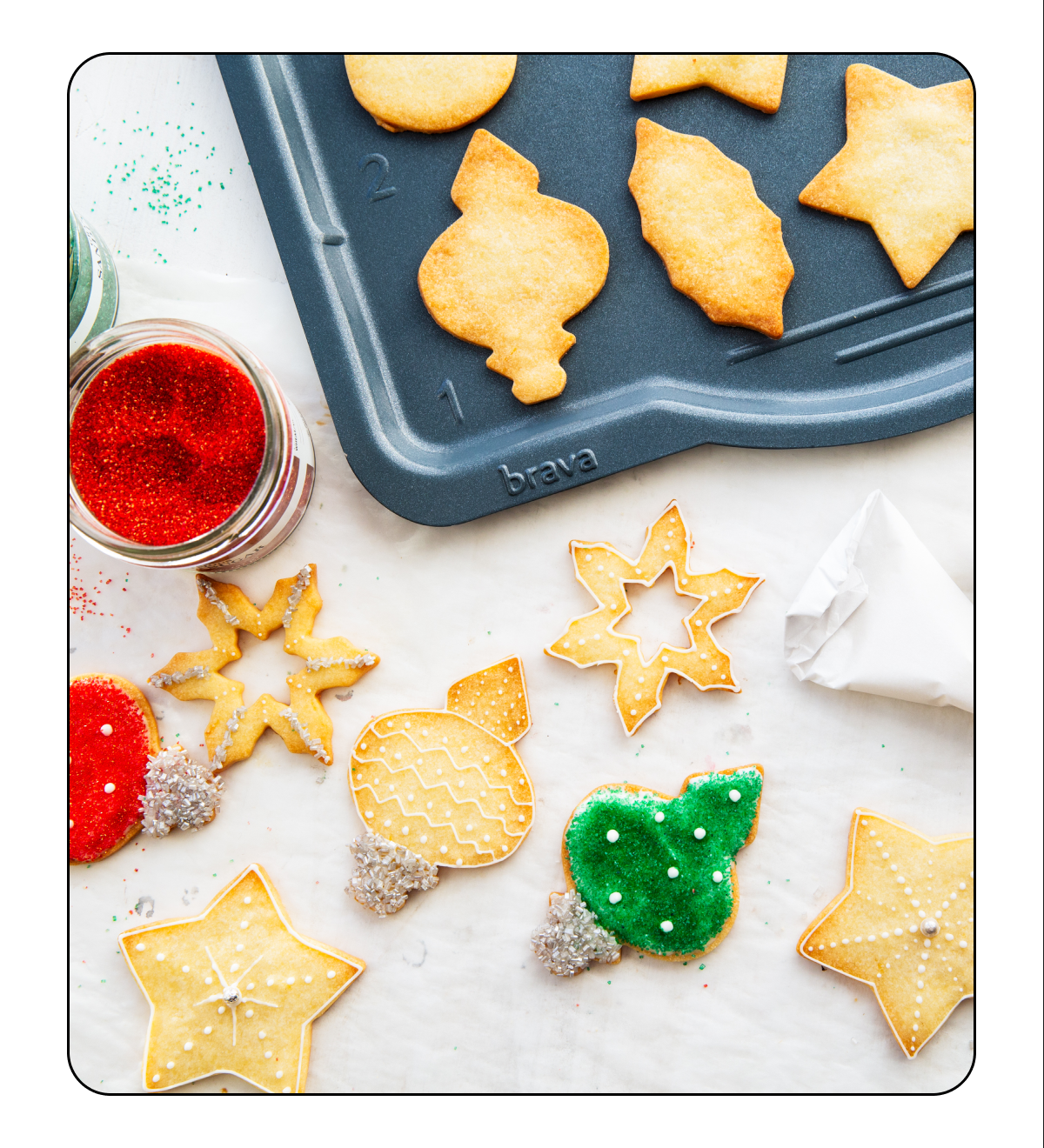 Colorfully decorated sugar cookies lay on a countertop next to a Brava Metal Tray holding undecorated cookies. What winter magic will you make with Brava?