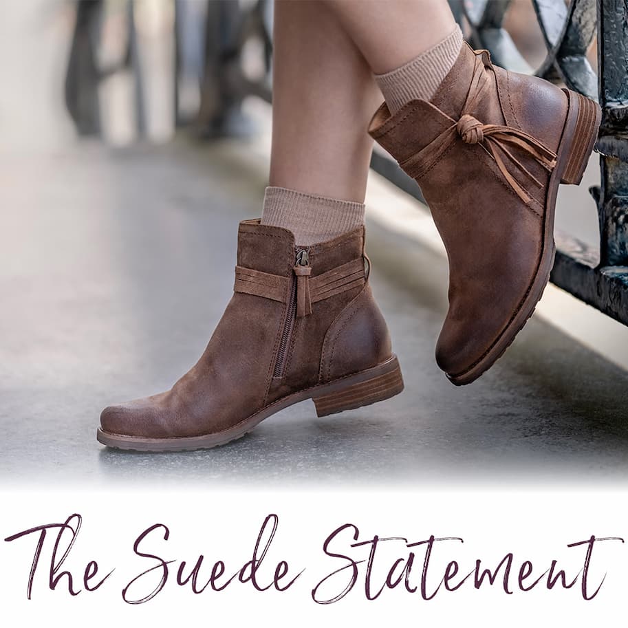 Sofft's Blake suede ankle boots in brown with side zipper and knotted strap detail, styled with neutral socks against an outdoor backdrop