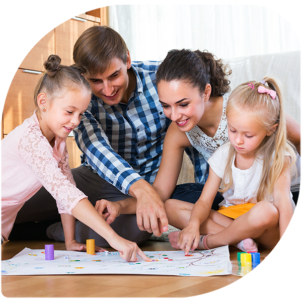 Happy young parents and two little daughters playing board game at home