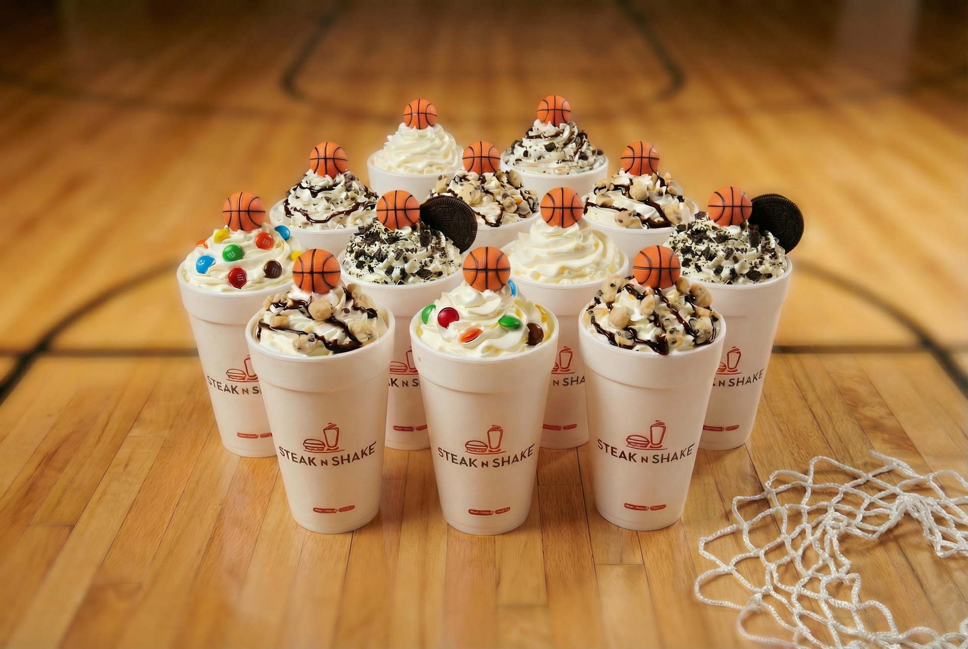12 milkshakes featuring basketballs instead of cherries on top bunched together on a wooden basketball court.