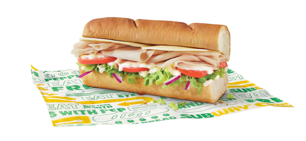A 6" turkey and cheese sub sits atop Subway-branded paper.