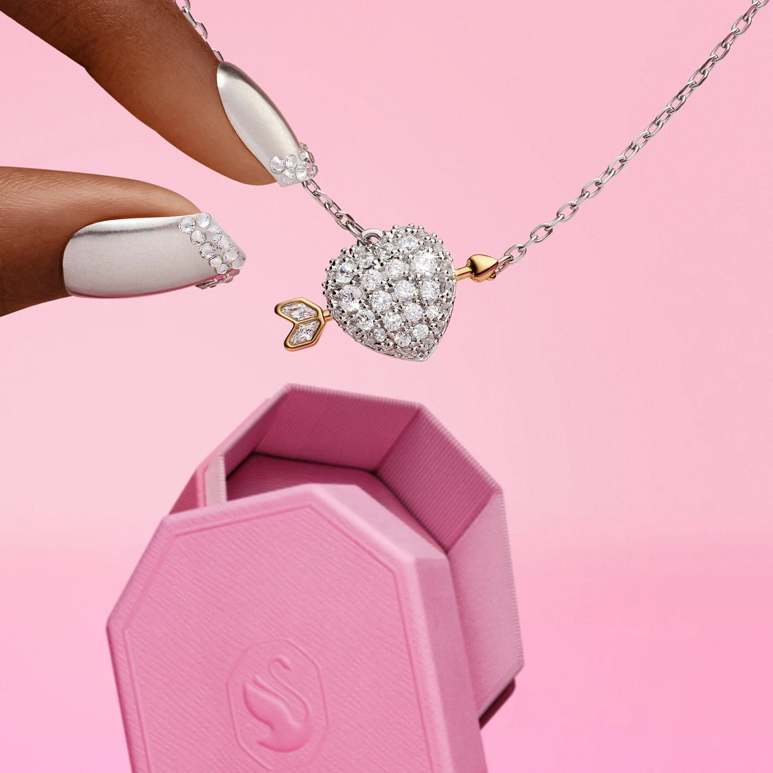 Fingers reaching for heart-shaped pendant