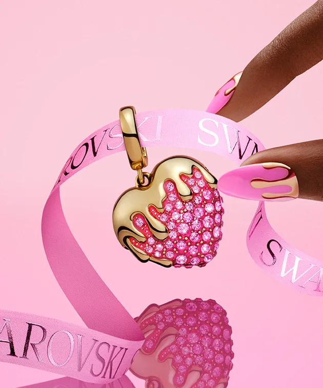 Fingers reaching for heart-shaped charm on pink background
