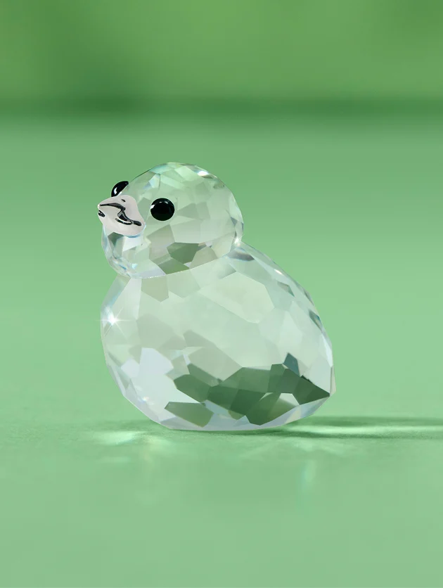 A small pheasant chick made of clear crystal, with shiny black eyes, set against a green background.