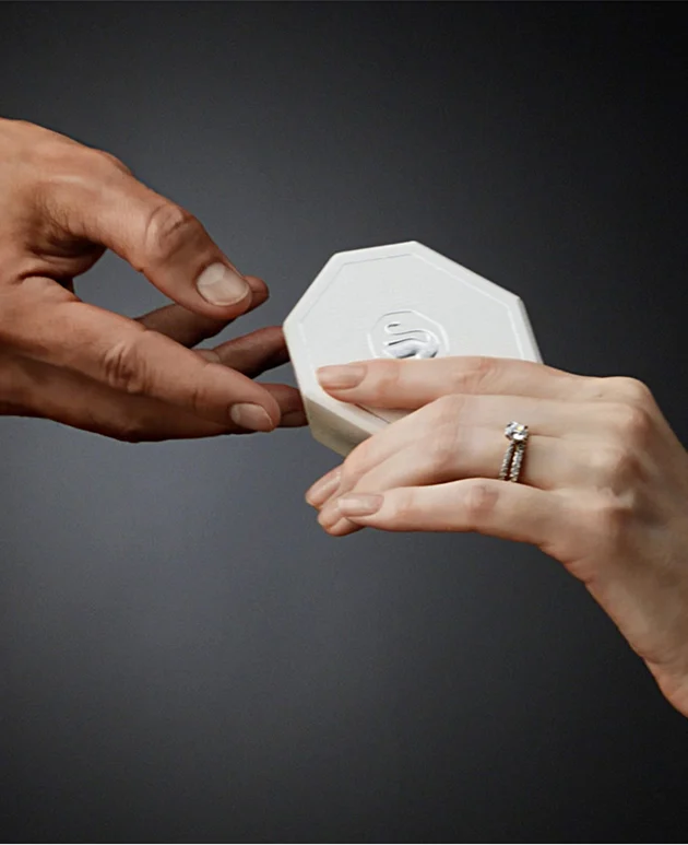 A hand wearing a Swarovski Created Diamonds ring gives a white Swarovski gift box to another hand