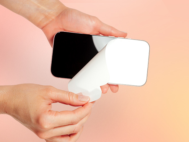 Hands peeling off the protective cover from a brand-new smartphone screen