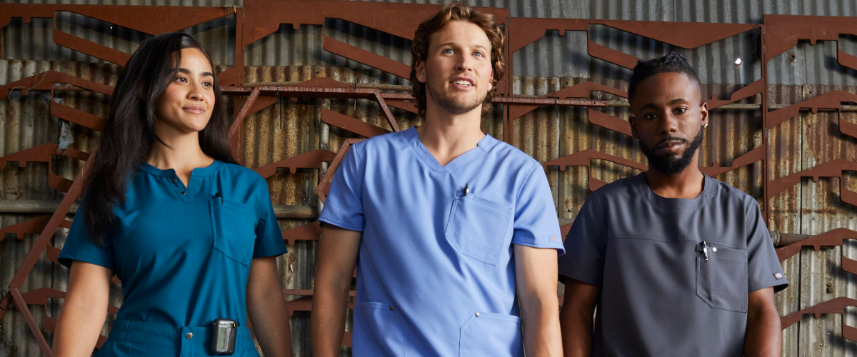 three people in blue Dickies scrubs standing in front of a brick wall