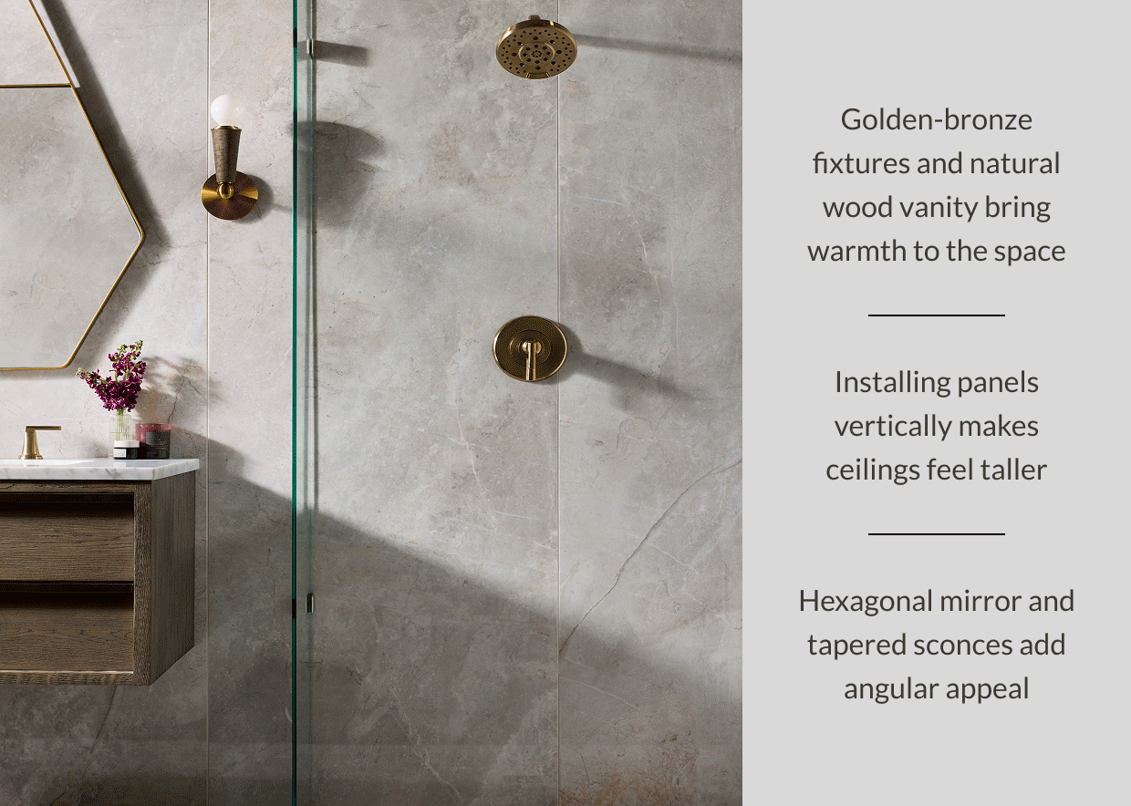 Golden-bronze fixtures and natural wood vanity bring warmth to the space. Installing panels vertically makes ceilings feel taller. Hexagonal mirror and tapered sconces add angular appeal