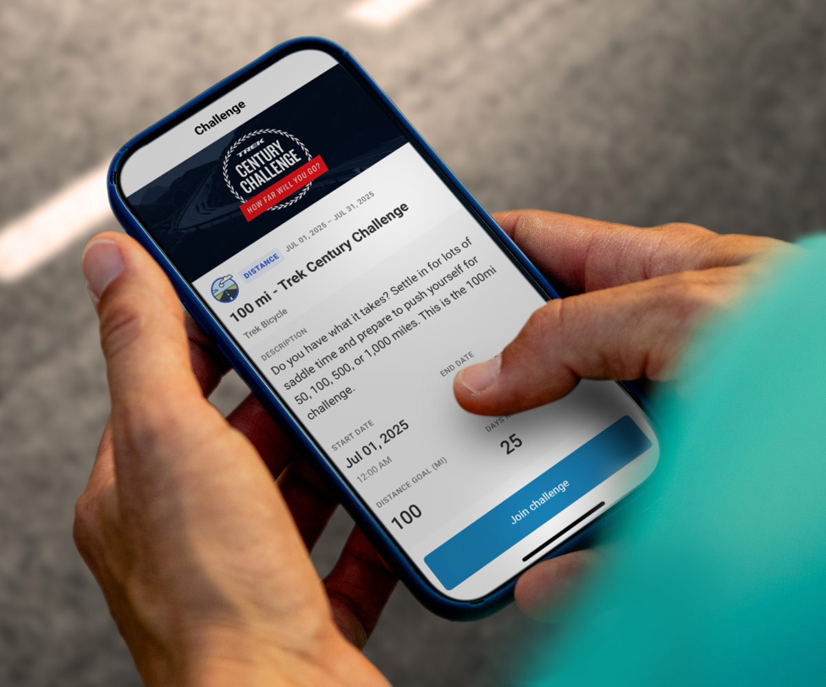 Cyclist looking at phone with screen displaying the Trek Century Challenge in the Ride Club app