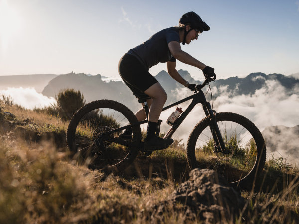 Cyclist wearing helmet while riding bike down mountain trail with clouds and mountain peaks in background