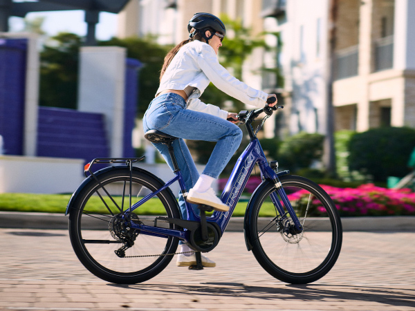 Cyclist wearing helmet while riding e-bike in city with buildings in background