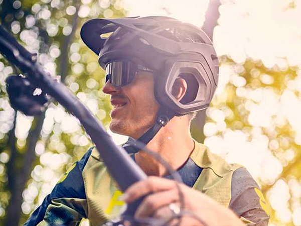 Cyclist wearing helmet and sunglasses while sitting on bike with trees and sun shining in background