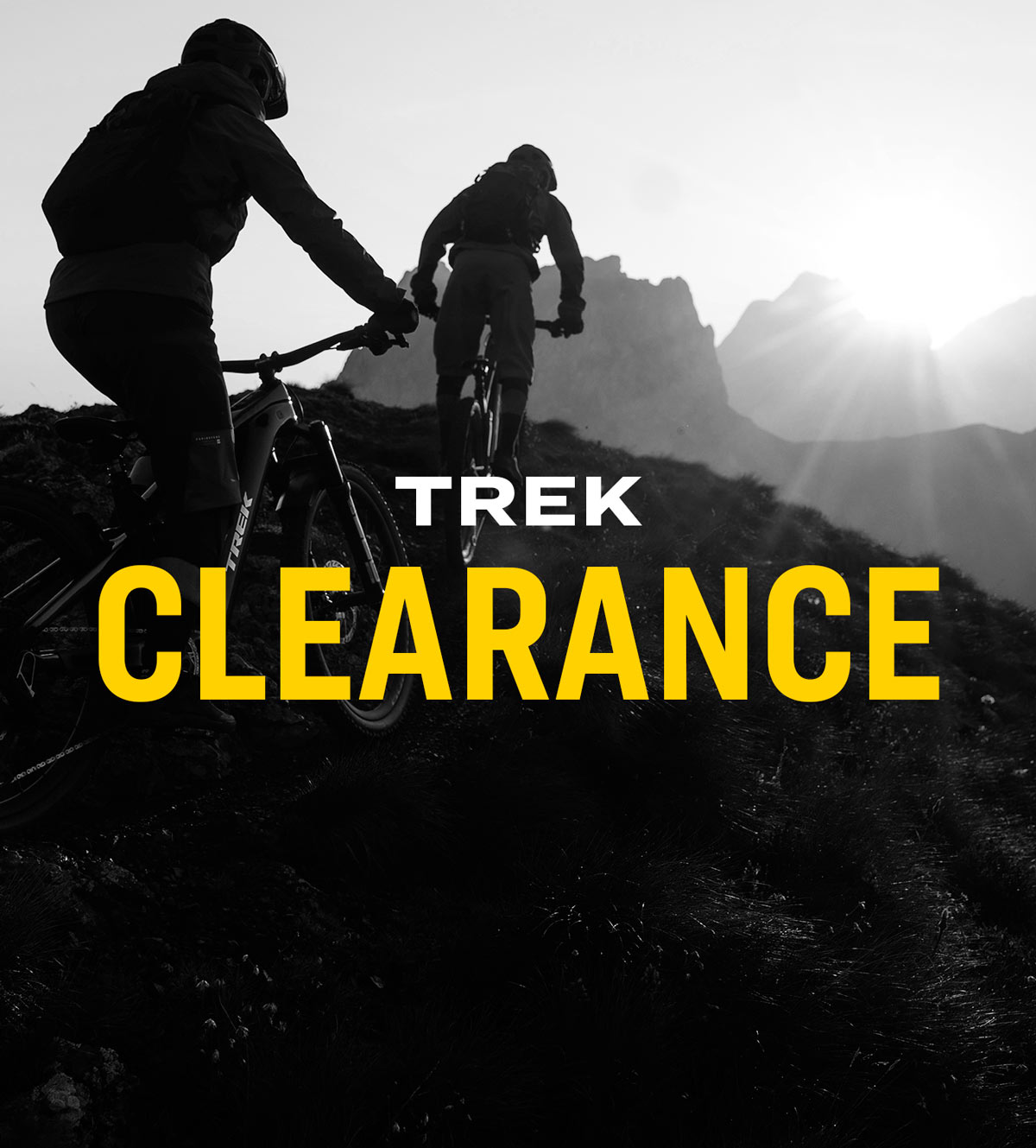 The words, 'TREK CLEARANCE' overlaying black and white photo of cyclists wearing helmets while riding bikes up mountain trail with sun shining over mountains in background